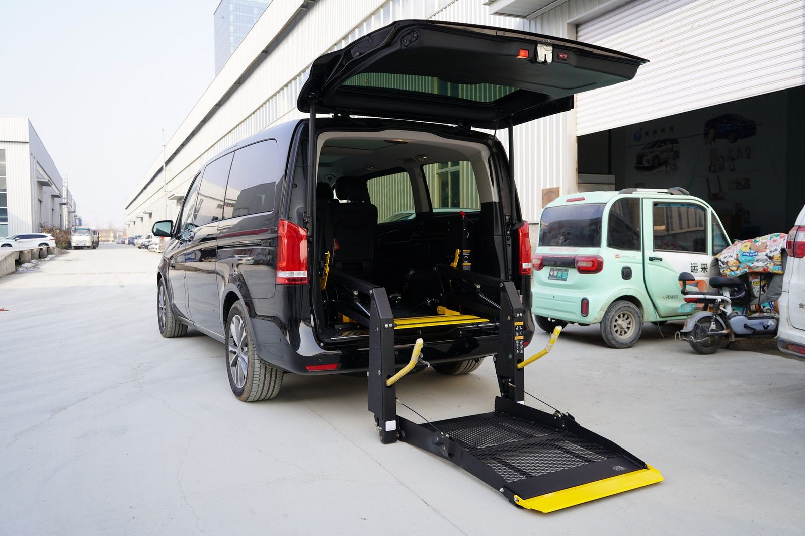 A black wheelchair-accessible van with its hydraulic side lift extended on a city street.
