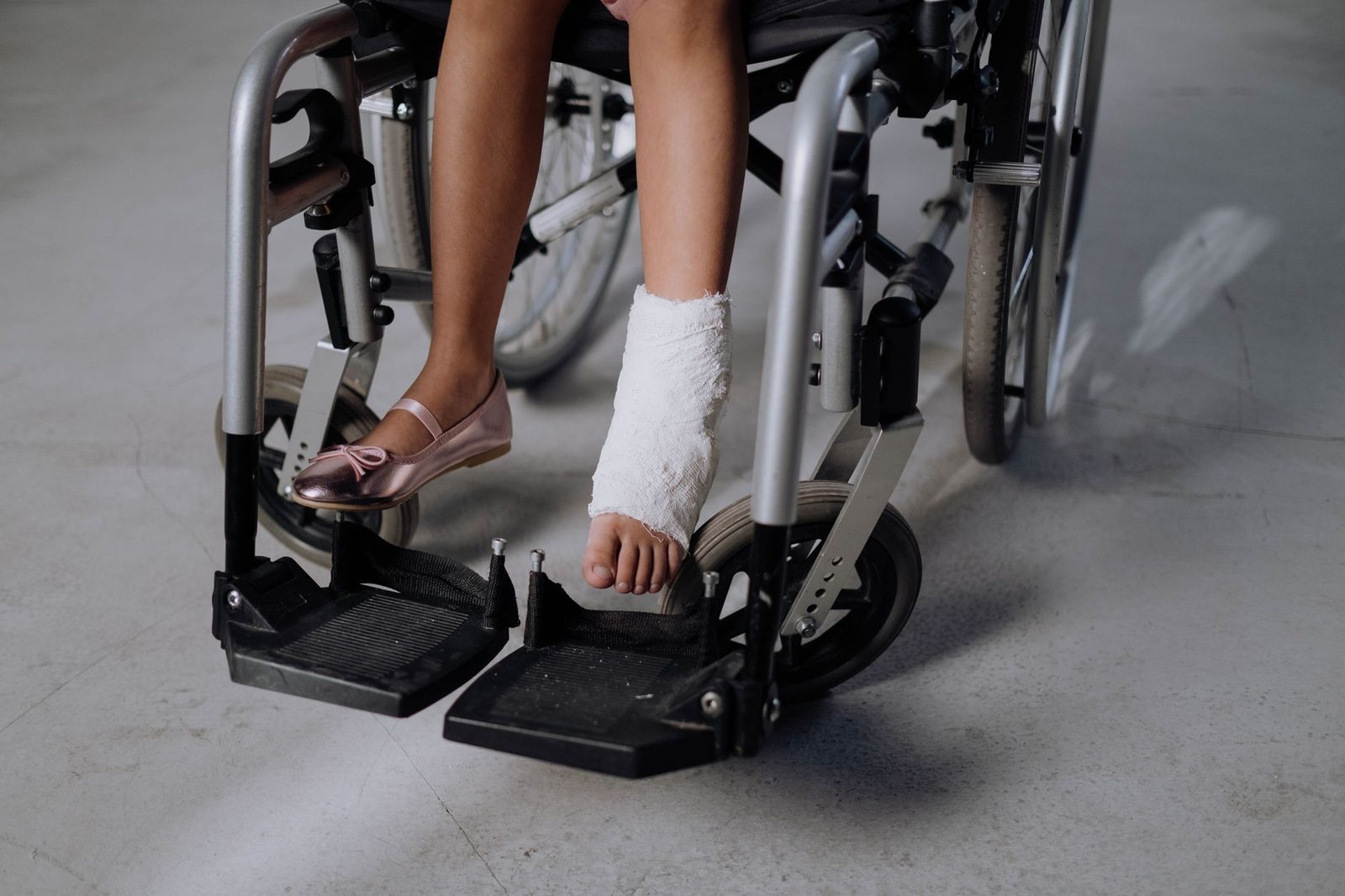 A close-up of a young girl's bandaged leg resting in a wheelchair.
