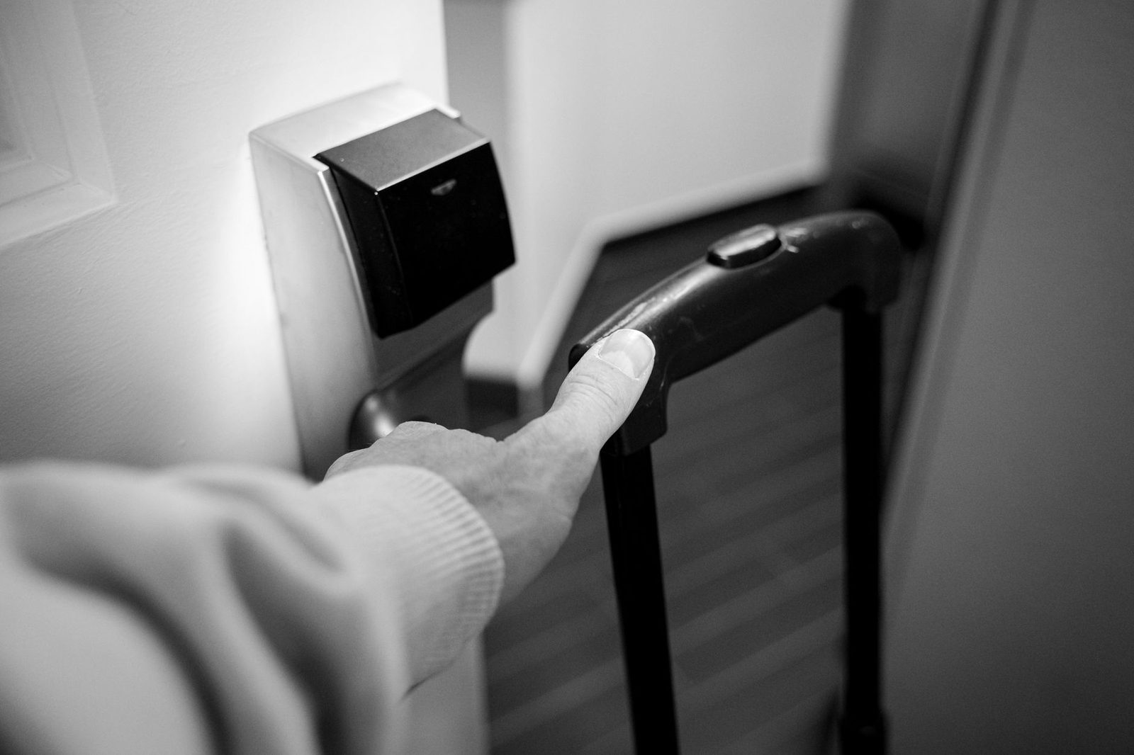 A monochrome photo of a hand opening a hotel room door while pulling a suitcase handle.