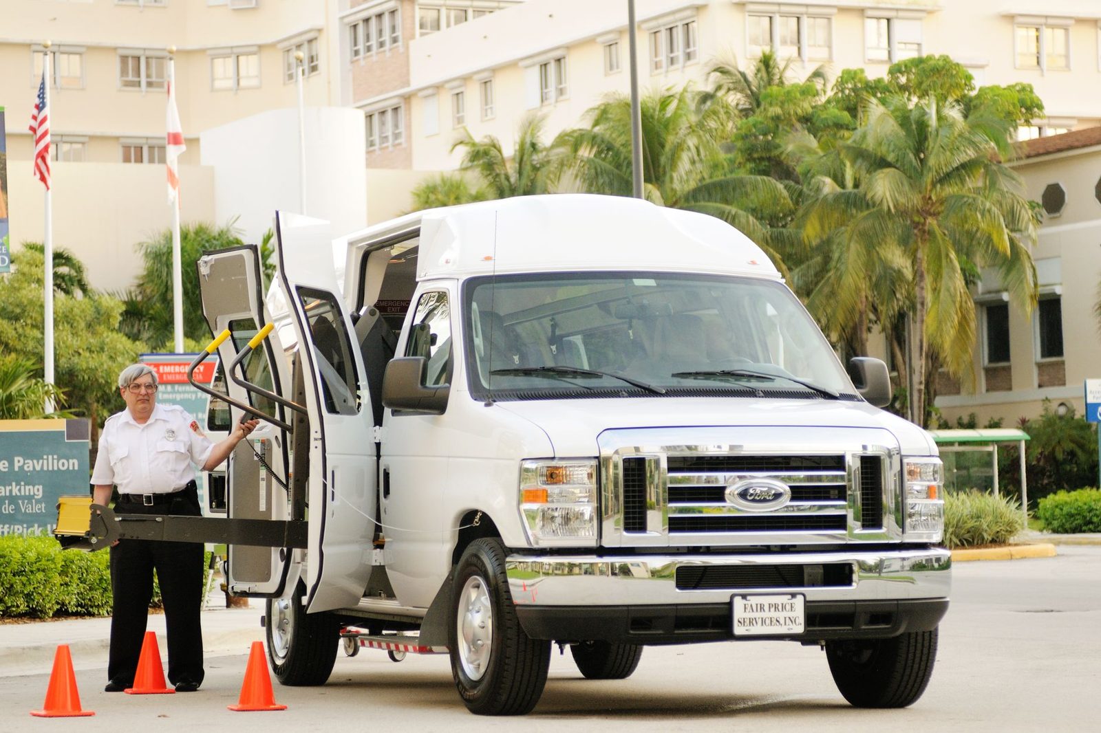 A parking attendant helps lower a wheelchair lift on a white van in a palm-lined lot.