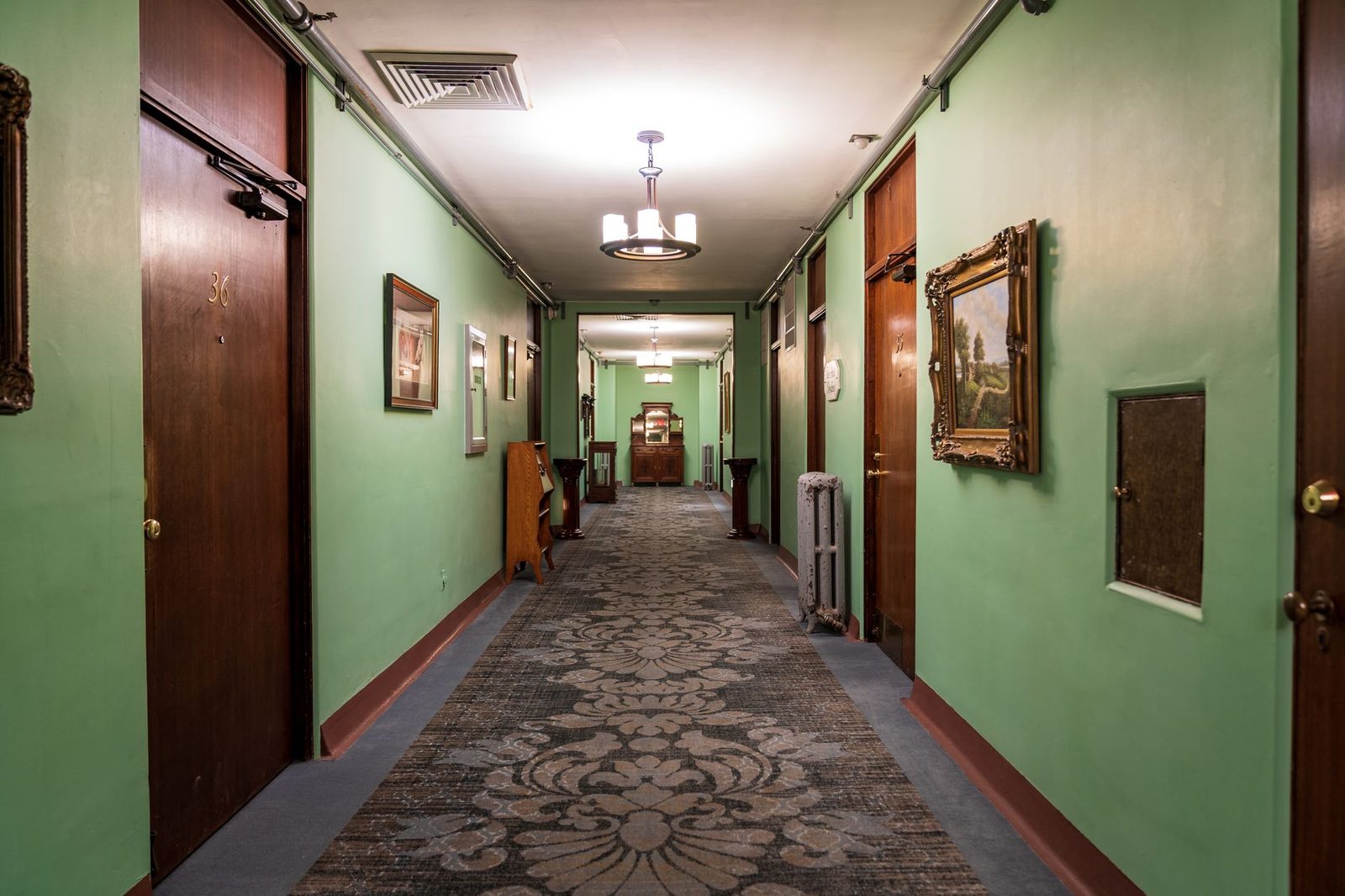 Pasillo tranquilo de un hotel antiguo con paredes verdes, puertas clásicas y cuadros enmarcados.