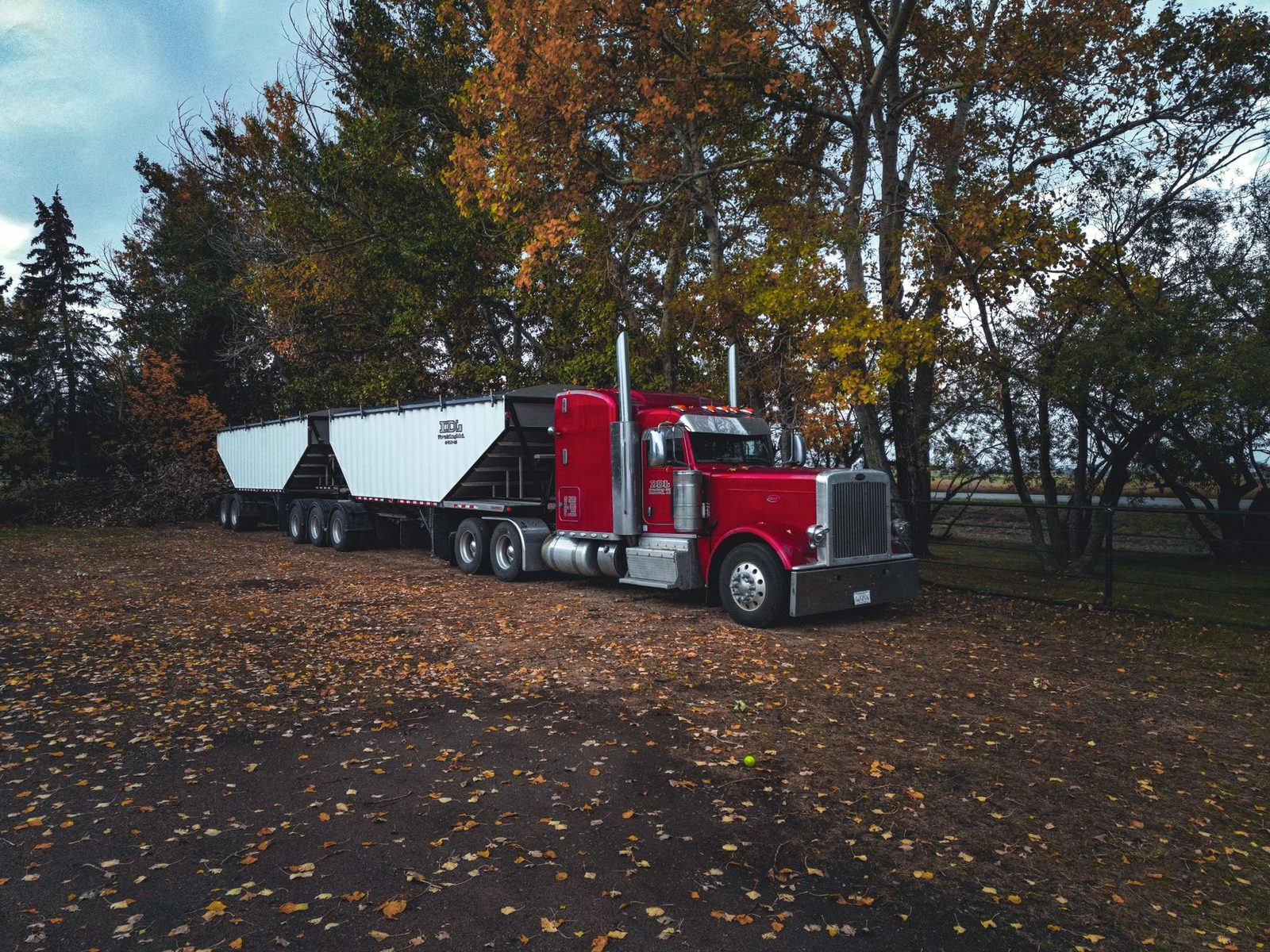 Un camión remolque rojo estacionado al aire libre entre árboles de otoño.