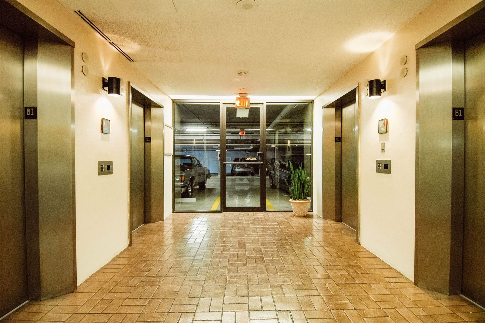 A well-lit parking garage lobby with several elevators and an illuminated exit sign.