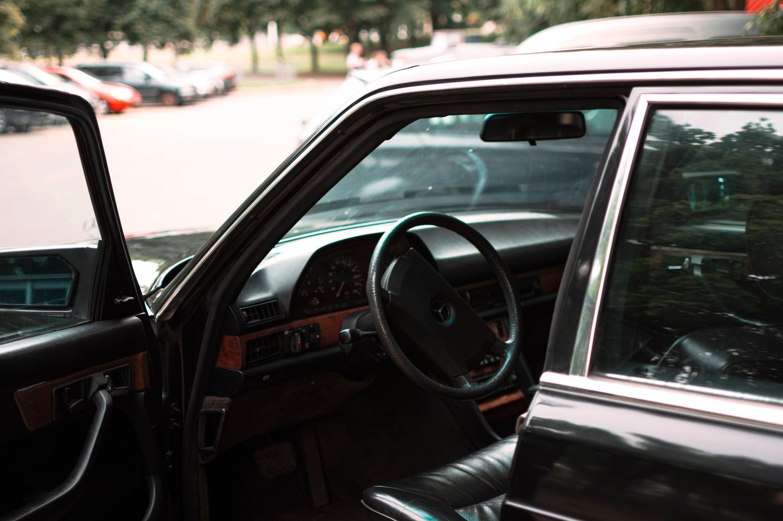 Close-up of a car's steering wheel and dashboard, seen through an open door, with a blurred parking lot behind.