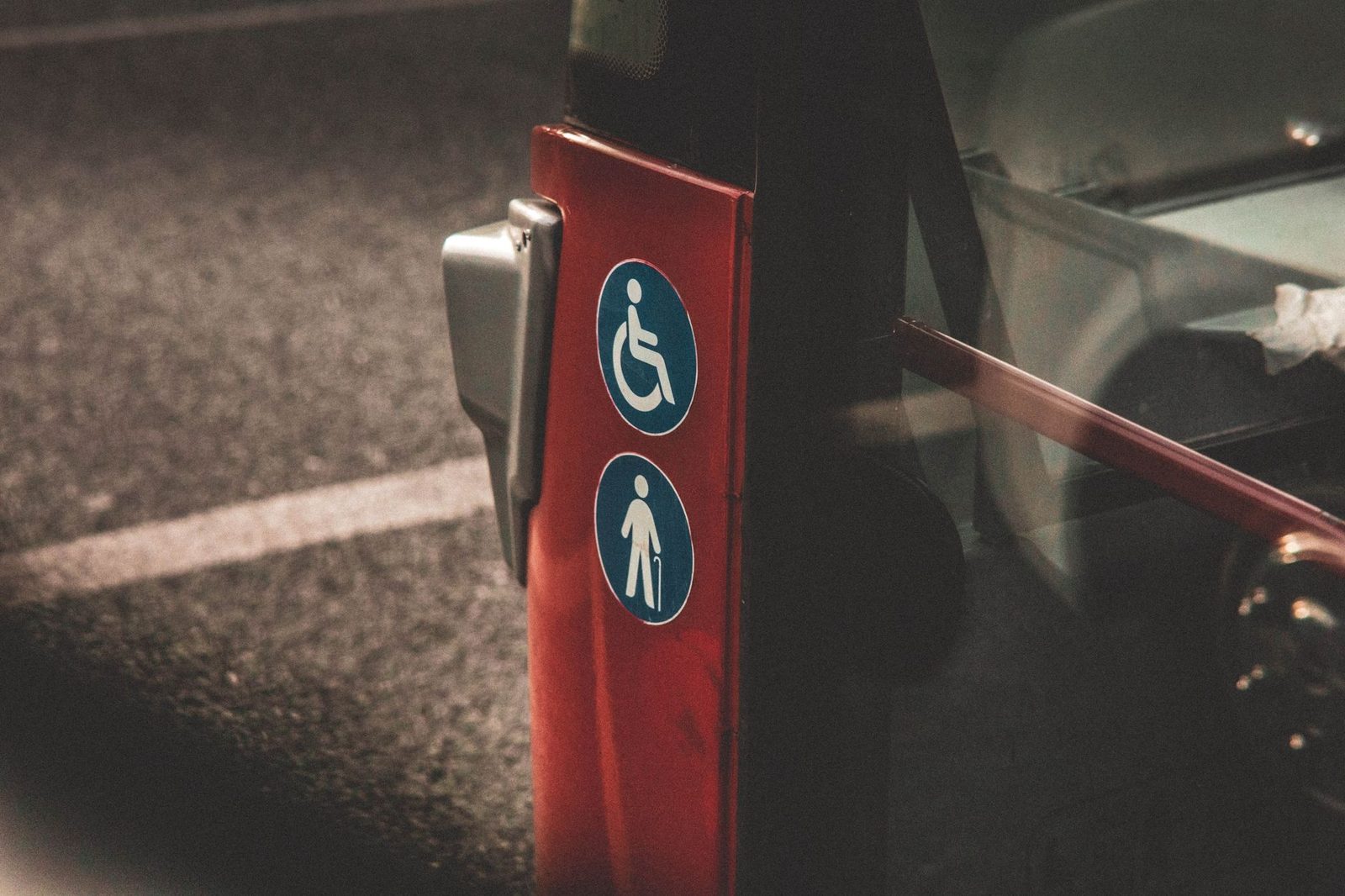 Primer plano de los símbolos de accesibilidad para sillas de ruedas y de prioridad para personas mayores en el costado de un autobús urbano rojo.
