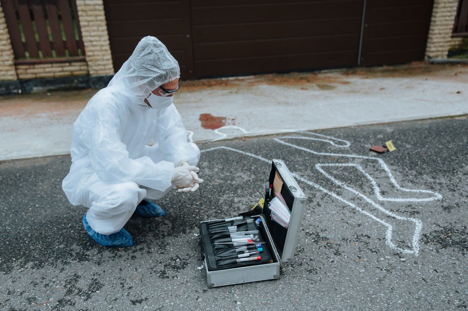 Crime scene investigator in protective gear examining evidence outdoors beside a case.