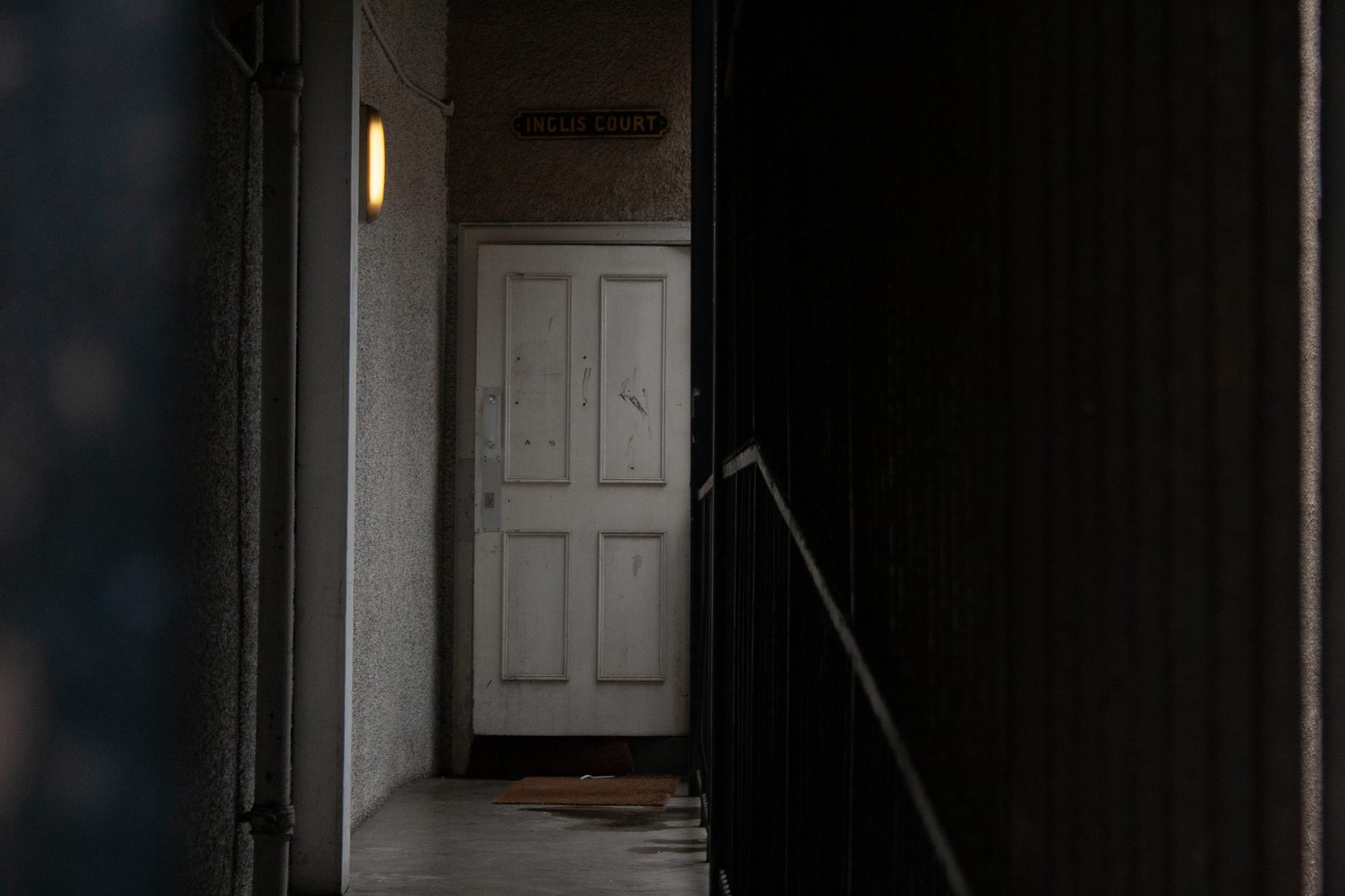 Dimly lit hallway with a closed wooden door at the end, creating an eerie, moody atmosphere.