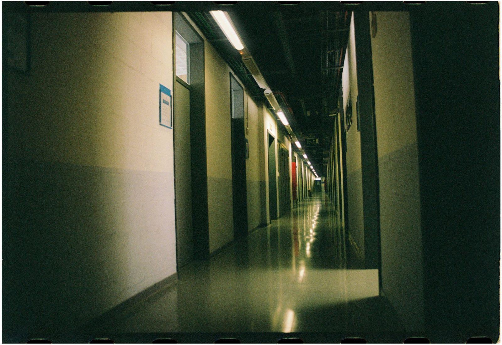Dimly lit industrial corridor stretching into the distance, shown in film-style perspective.