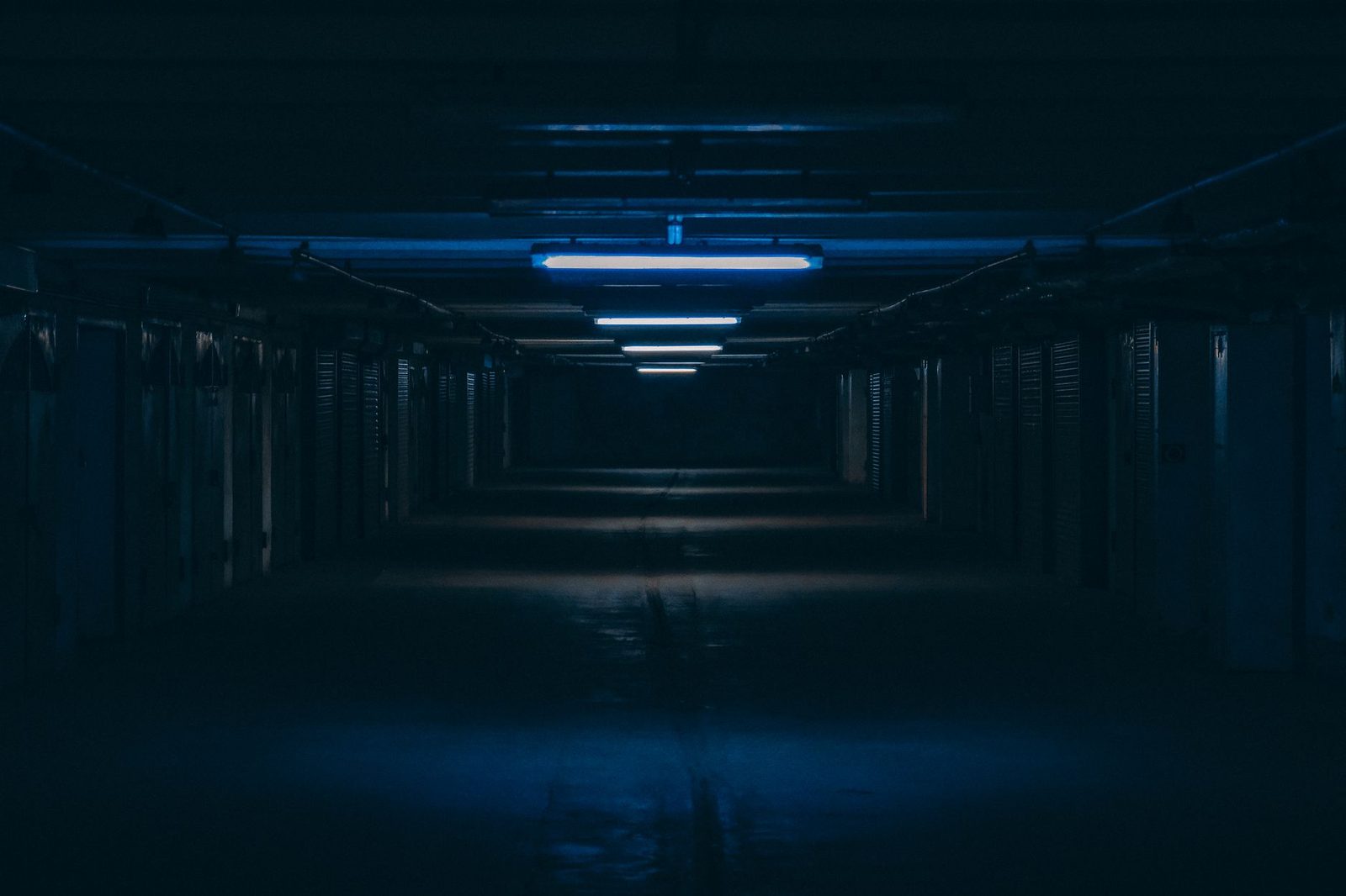Dimly lit underground parking garage with concrete pillars and an eerie, shadowy atmosphere.