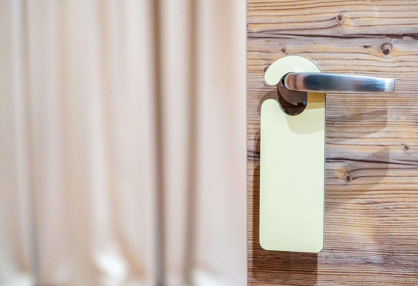 Puerta de madera elegante con manija de acero inoxidable y una etiqueta de habitación de hotel.