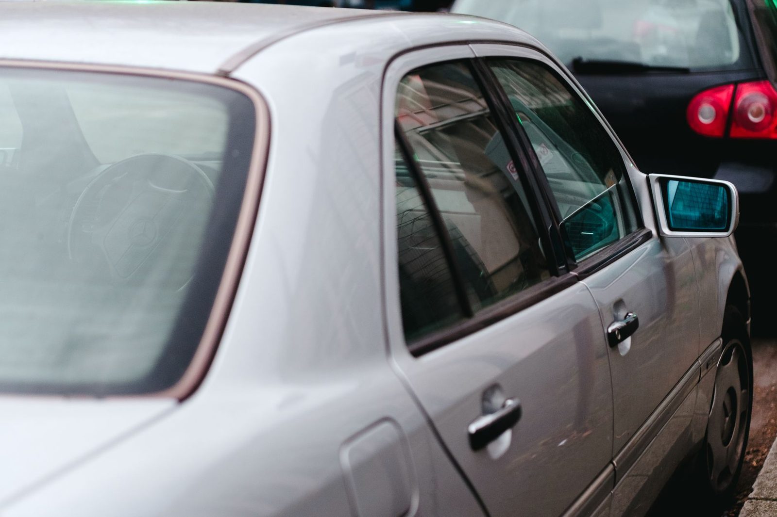 Silver car parked on a city street, seen from the side with a reflection in the window.