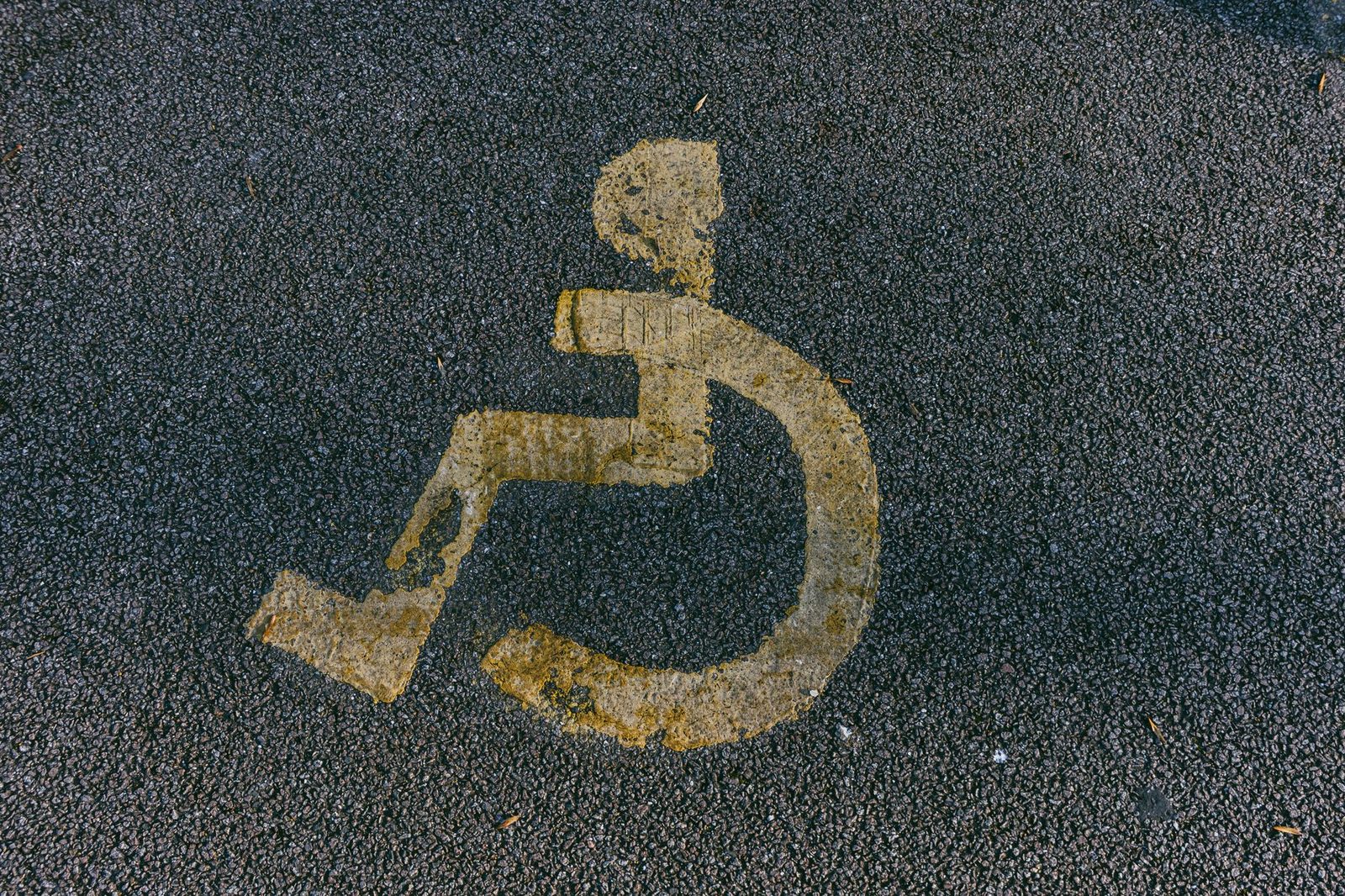 Símbolo de silla de ruedas pintado y desgastado sobre el asfalto en una plaza de estacionamiento para personas con discapacidad.