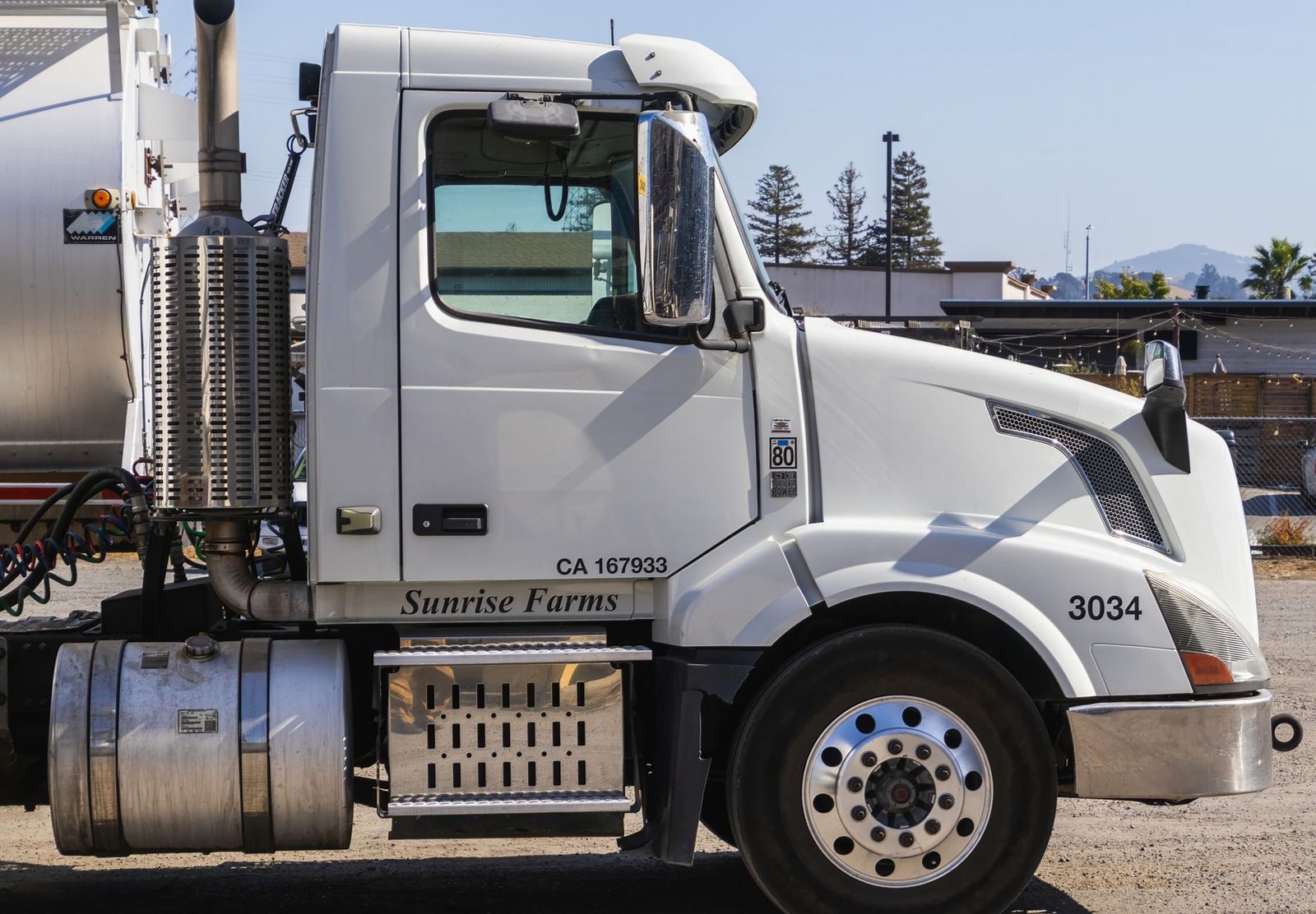 White semi-trailer truck parked outdoors in an industrial area, shown from the side.
